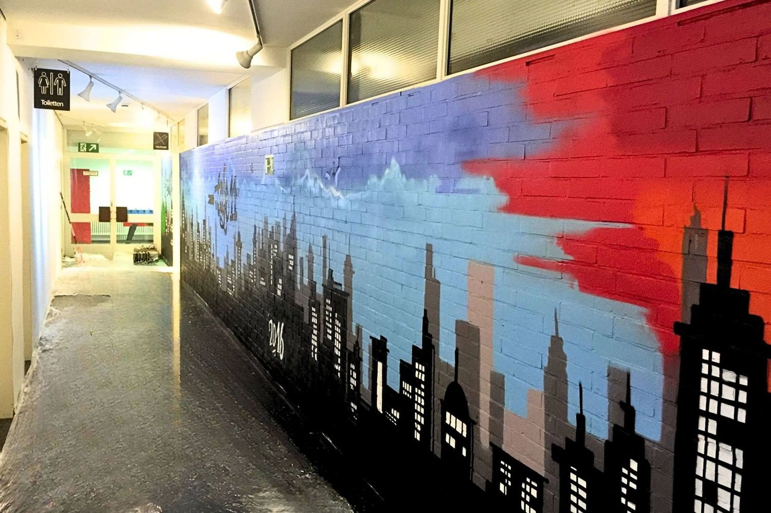 Graffiti Skyline mit Sonnenuntergang in Schulflur – Stadtbild auf roter Backsteinwand