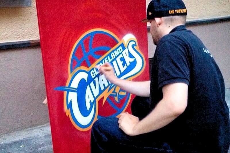 Graffiti Künstler gestaltet Cleveland Cavaliers Logo per Spraydose auf rotem Hintergrund
