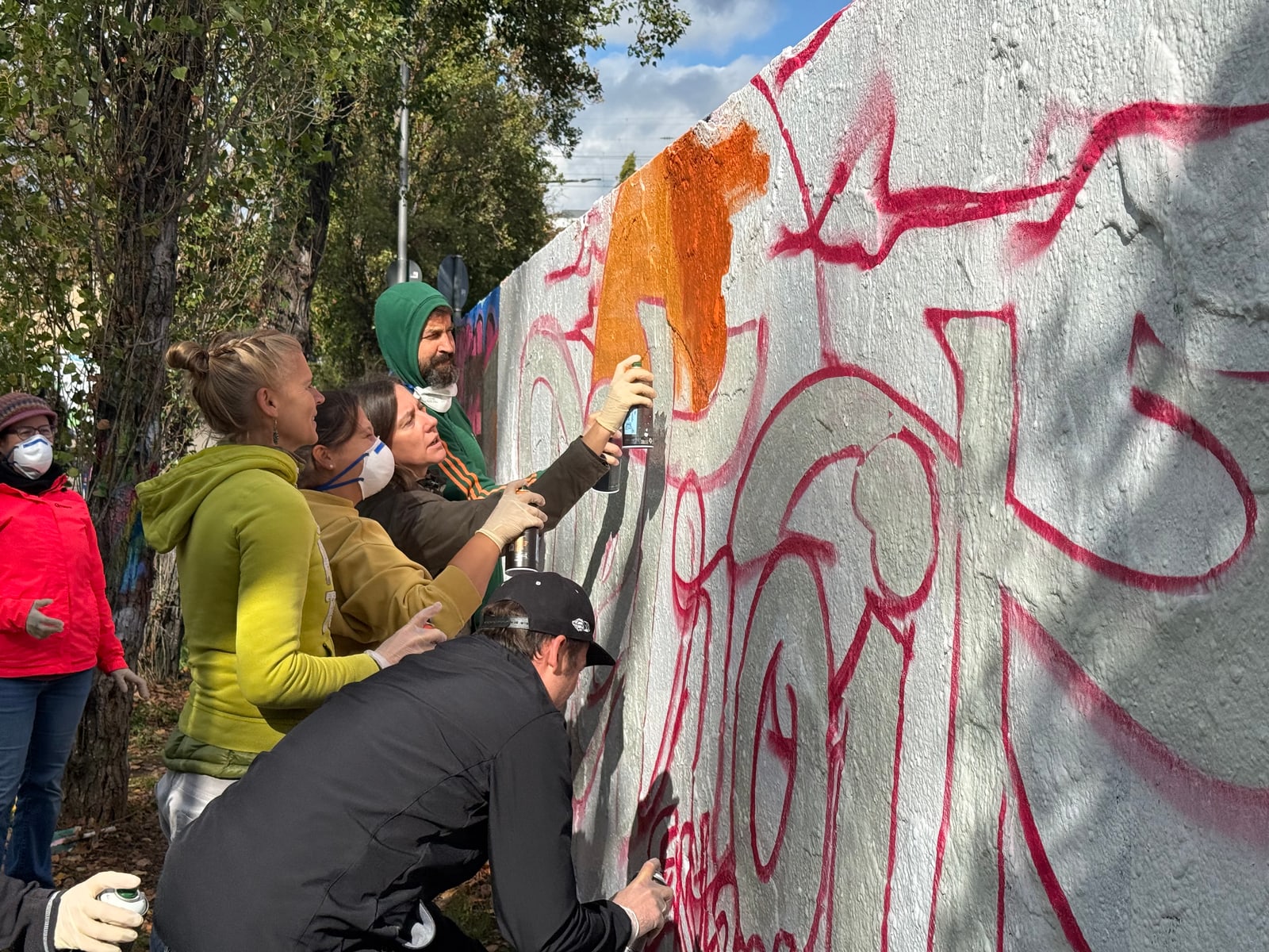 Mehrere Teilnehmende mit Handschuhen und Atemschutz sprühen dicht nebeneinander an derselben Stelle der Wand.