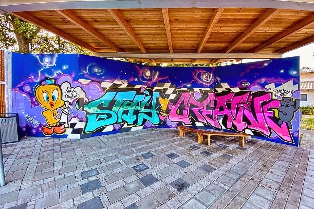 Fertiges Graffiti mit dem Schriftzug „Stay Creative“ vor galaktischem Hintergrund mit Charakteren, gesprüht am neuen Jugendunterstand in Ditzingen.