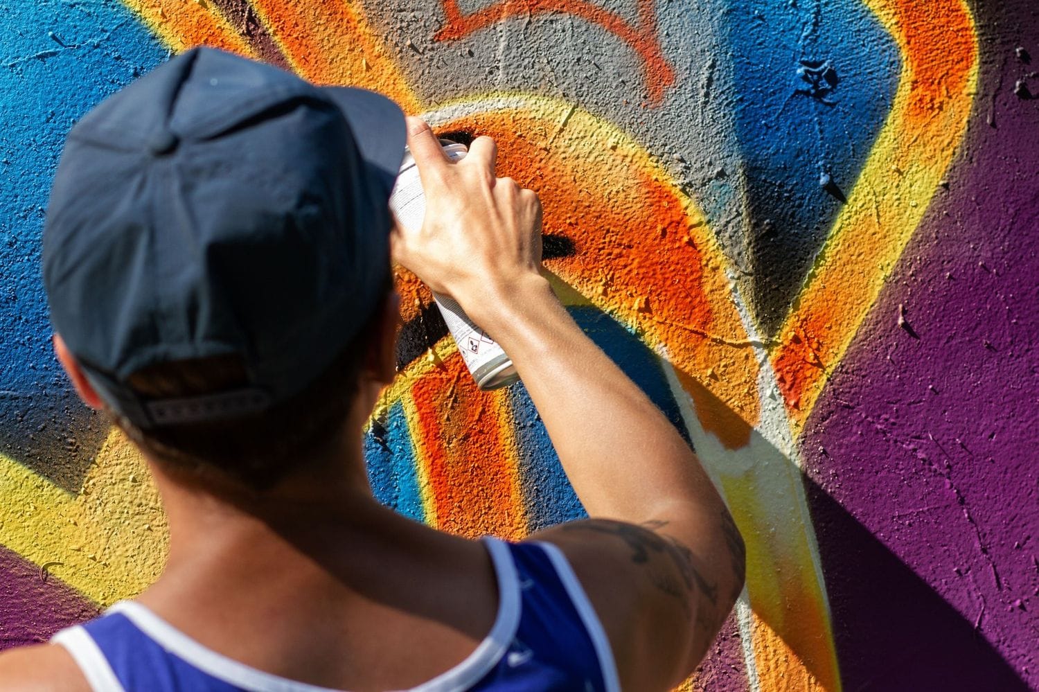 Workshopteilnehmer sprüht mit Cap und Dose ein buntes Graffiti auf eine Wand.