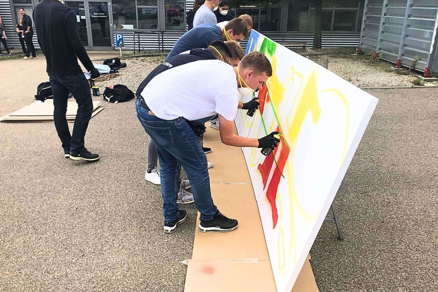 Teilnehmer:innen beim Graffiti-Workshop in Stuttgart sprayen gemeinsam ein großes Graffiti auf Leinwand..