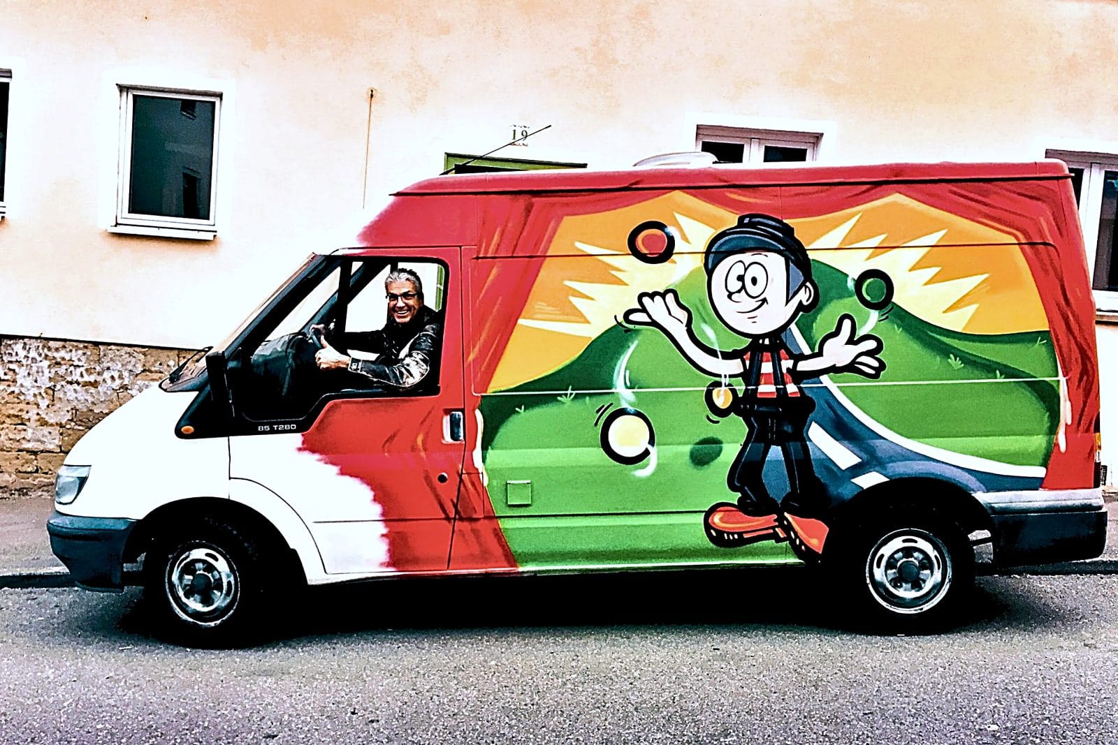 Vollflächig gestalteter Ford-Transit-Bus mit Cartoon-Jongleur als Fahrzeug-Graffiti von Open Mike