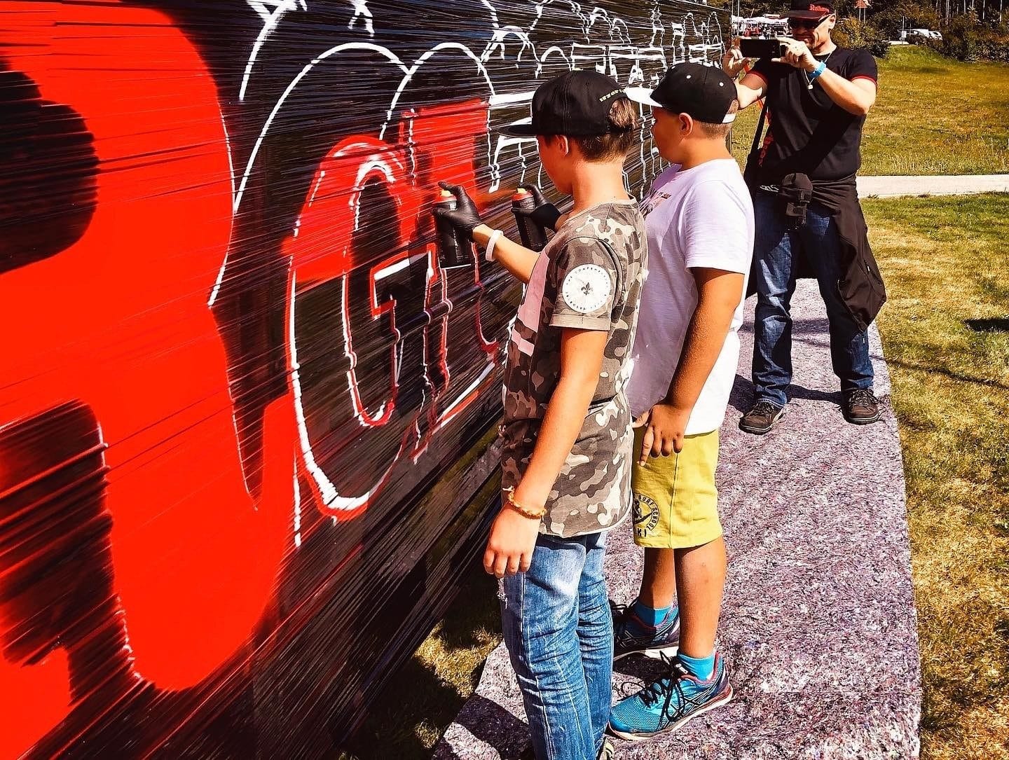 Workshop-Gruppe vor dem gemeinsam gesprühten Graffiti von Open Mike