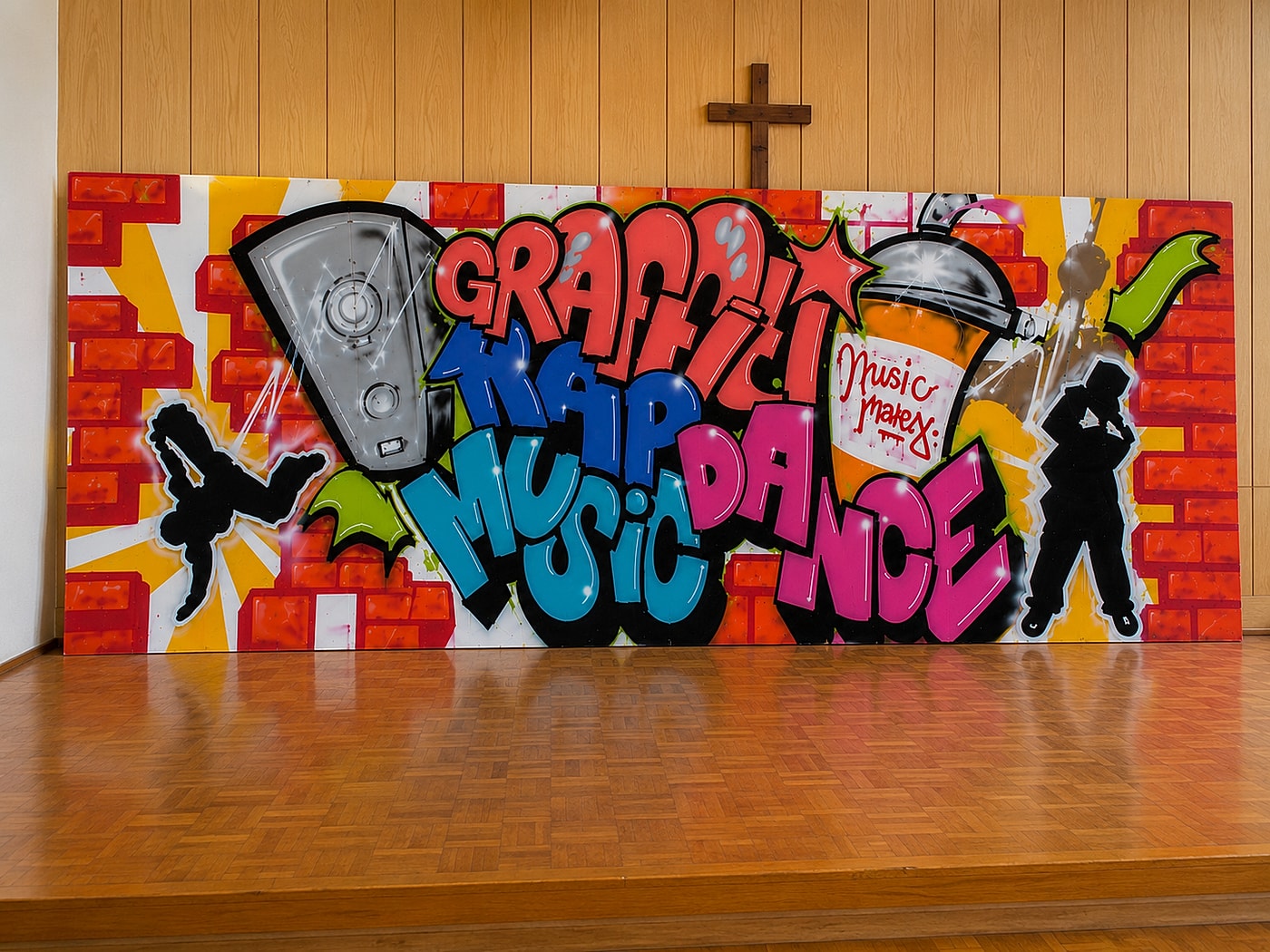 Zwei bemalte Holzplatten (je 2×2 m) mit dem Graffiti »Graffiti · Rap · Music · Dance«, für das Foto im Gemeinderaum der Apis aufgestellt