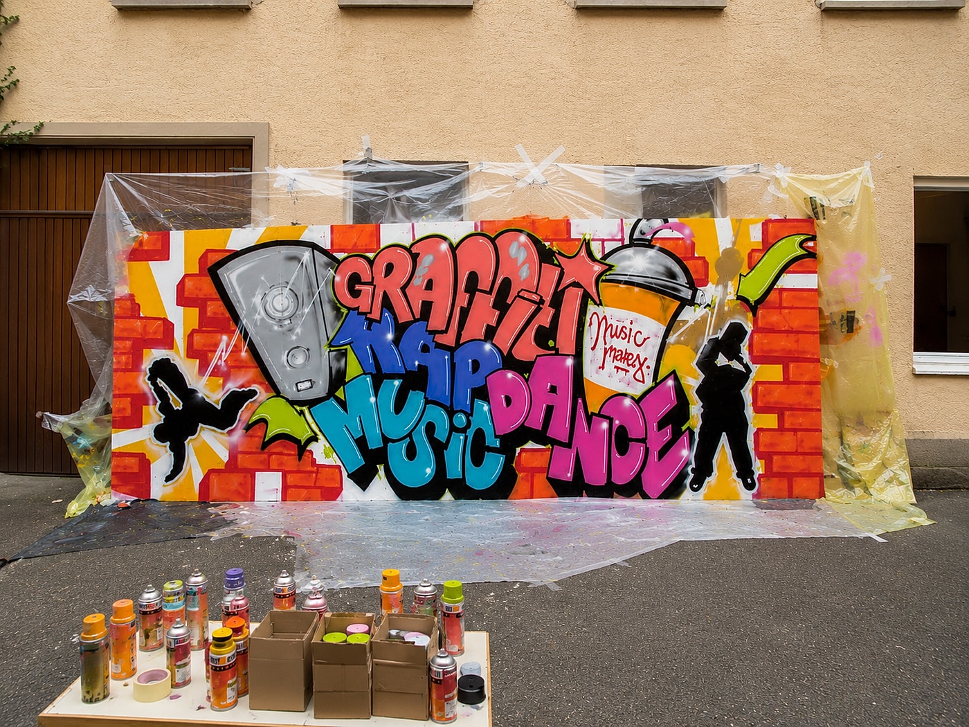 Die zwei Graffiti-Holzplatten beim Entstehen draußen im Hof – mit Sprühdosen und Material davor