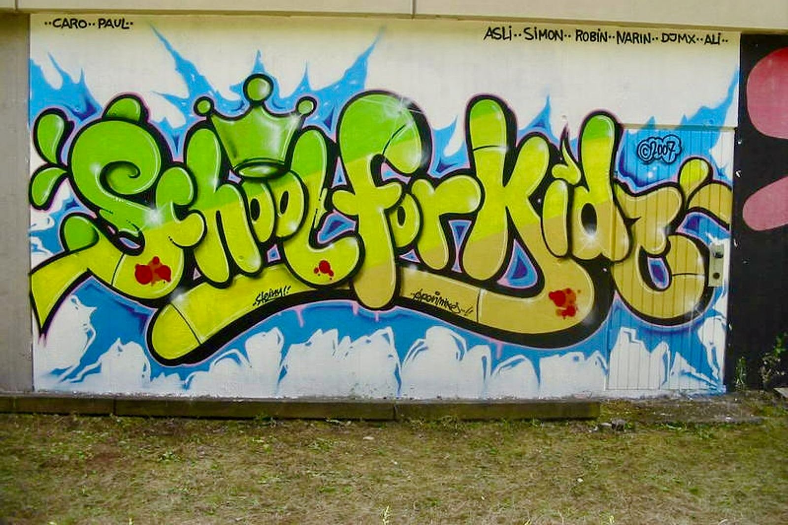 Fertiges Graffiti-Piece mit gelb-grünem »Kids«-Schriftzug und blauen Highlights an der Schulwand