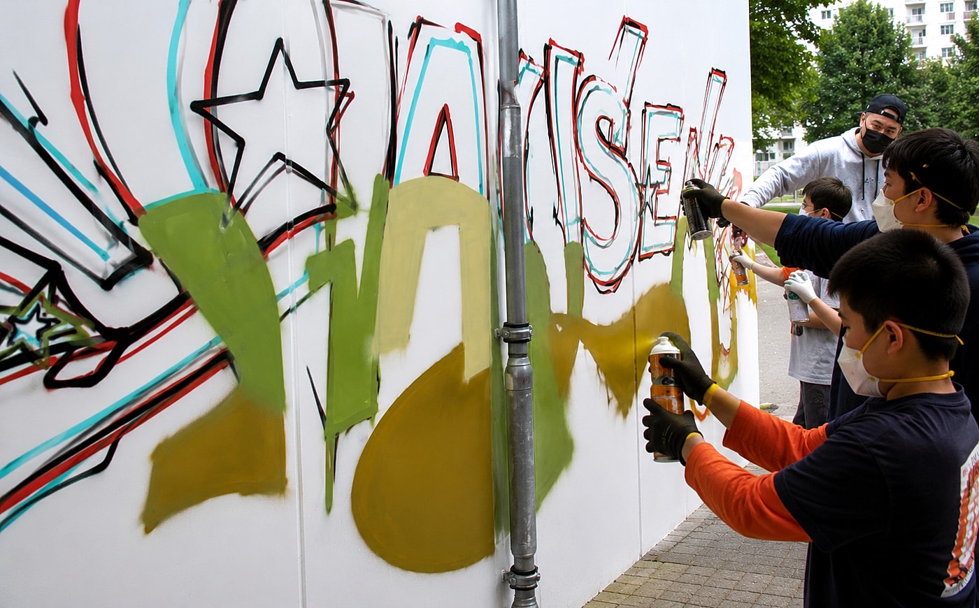Nahaufnahme: Teilnehmer sprüht die goldene Füllung des Graffiti-Schriftzugs