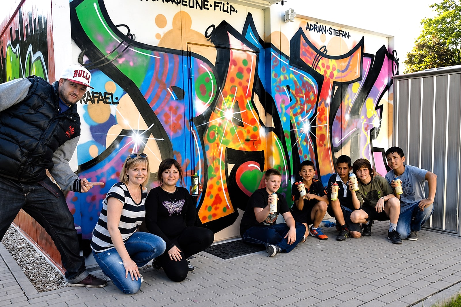 Coach Open Mike mit der Workshop-Gruppe vor dem fertigen »Party«-Graffiti am Jugendhaus Mosbach, alle mit Sprühdosen in der Hand