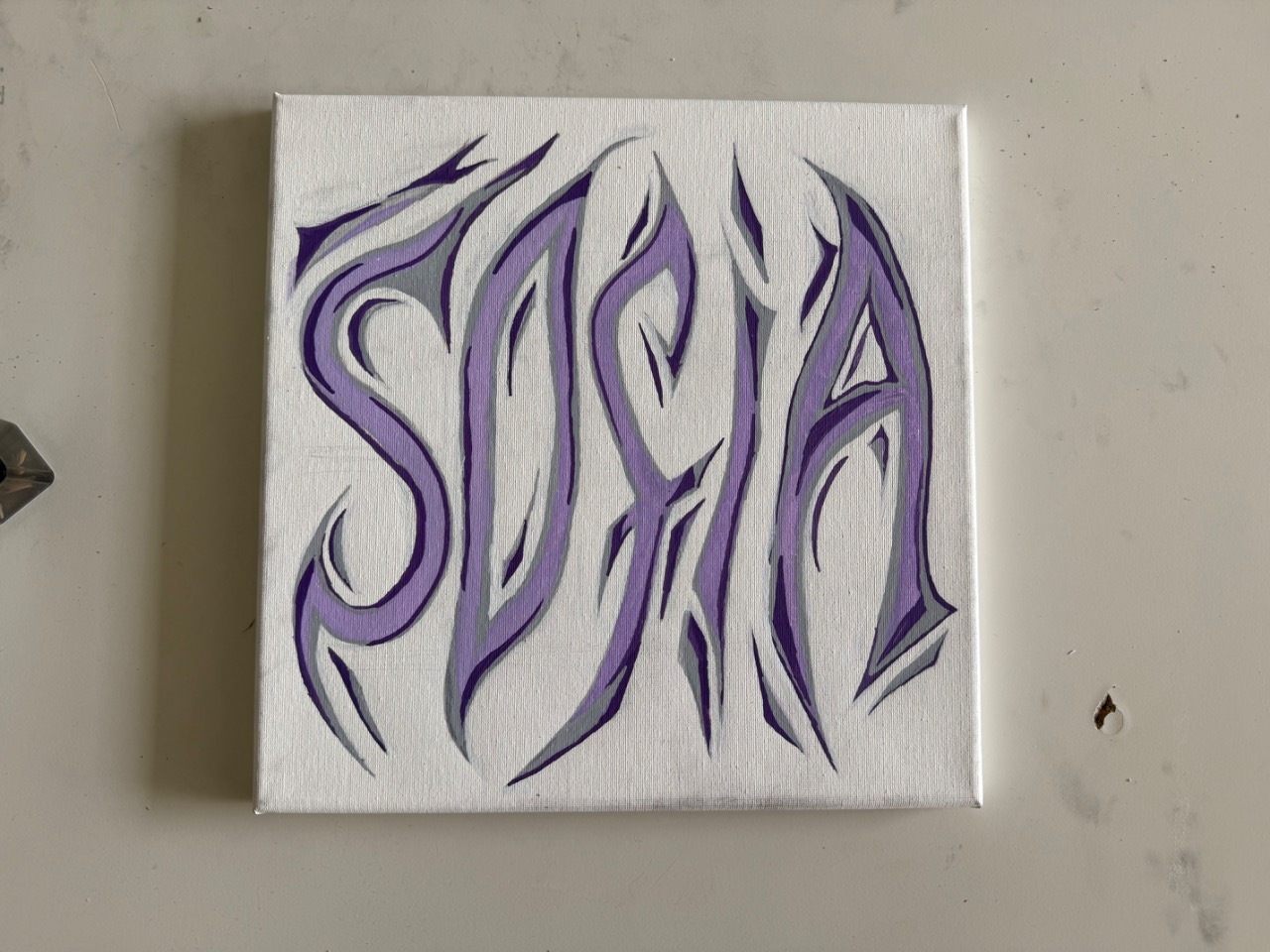 Weiße Leinwand auf grauem Untergrund mit dem Schriftzug Sofia in lila und grauen Graffiti-Buchstaben mit spitzen, flammenartigen Ausläufern.