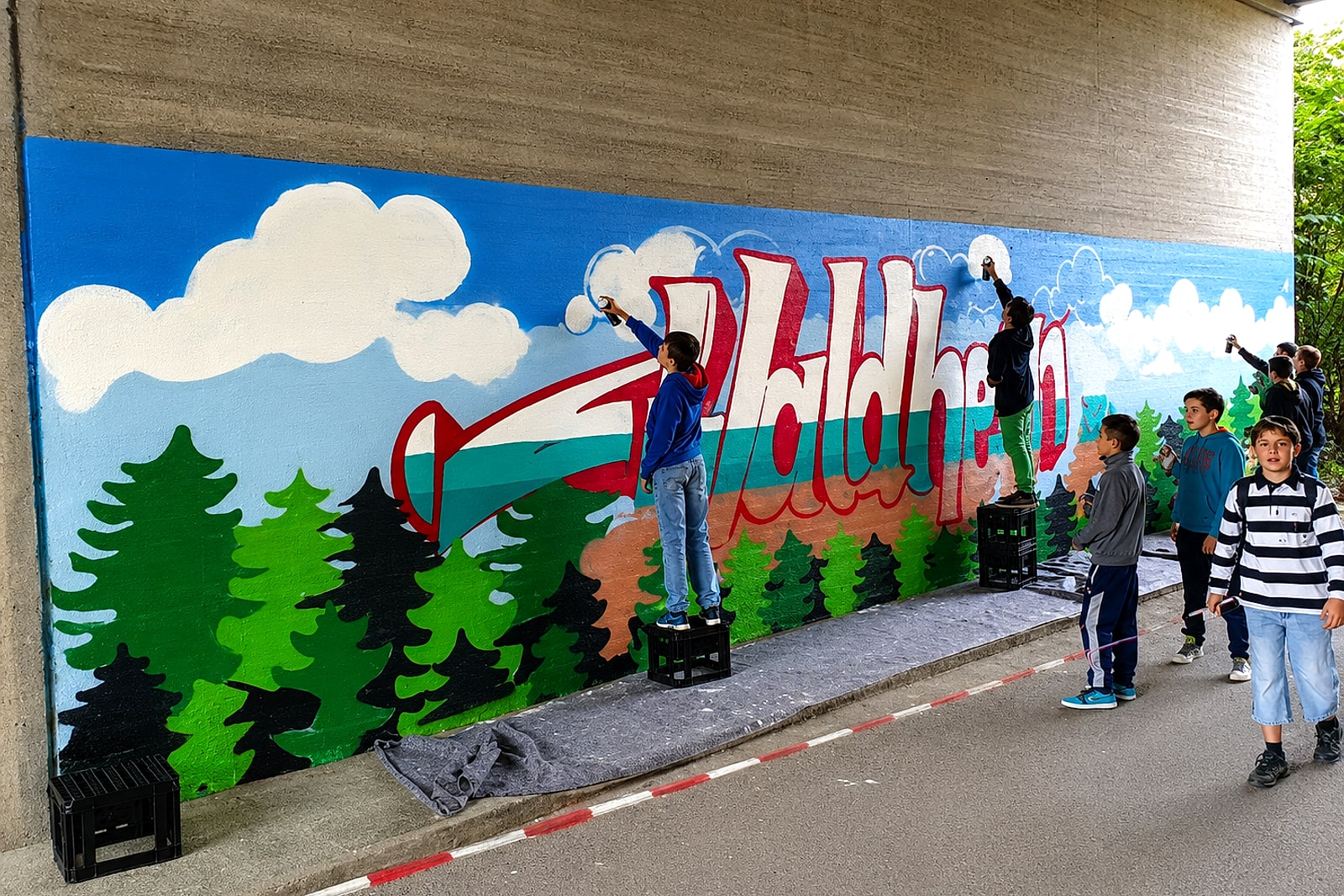Kinder stehen auf Getränkekisten und gestalten gemeinsam das »Waldheim«-Graffiti an der Unterführungswand in Stuttgart-Möhringen.