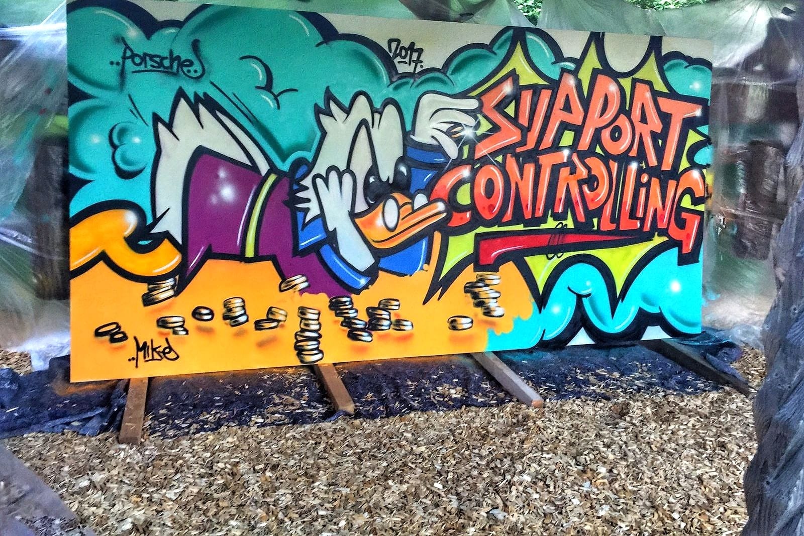 Live-Graffiti-Werk Support Controlling mit Comic-Motiv und Goldmuenzen beim Porsche-Teamevent in Weissach von Open Mike